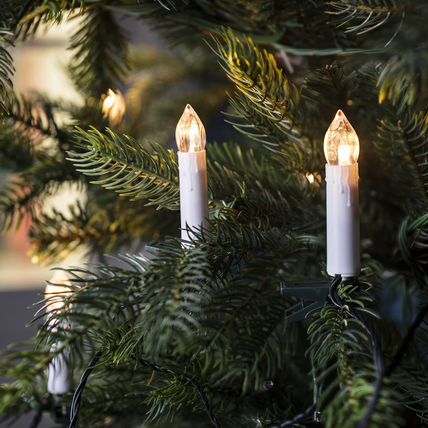 Warmweiße LED Weihnachtsbaumkerzen an den Zweigen eines Weihnachtsbaumes